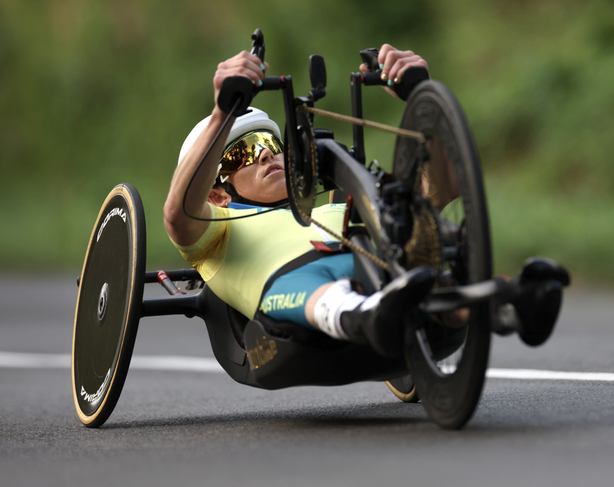 A para athlete wearing a yellow racing top and helmet powers a handcycle down a road during competition. The athlete